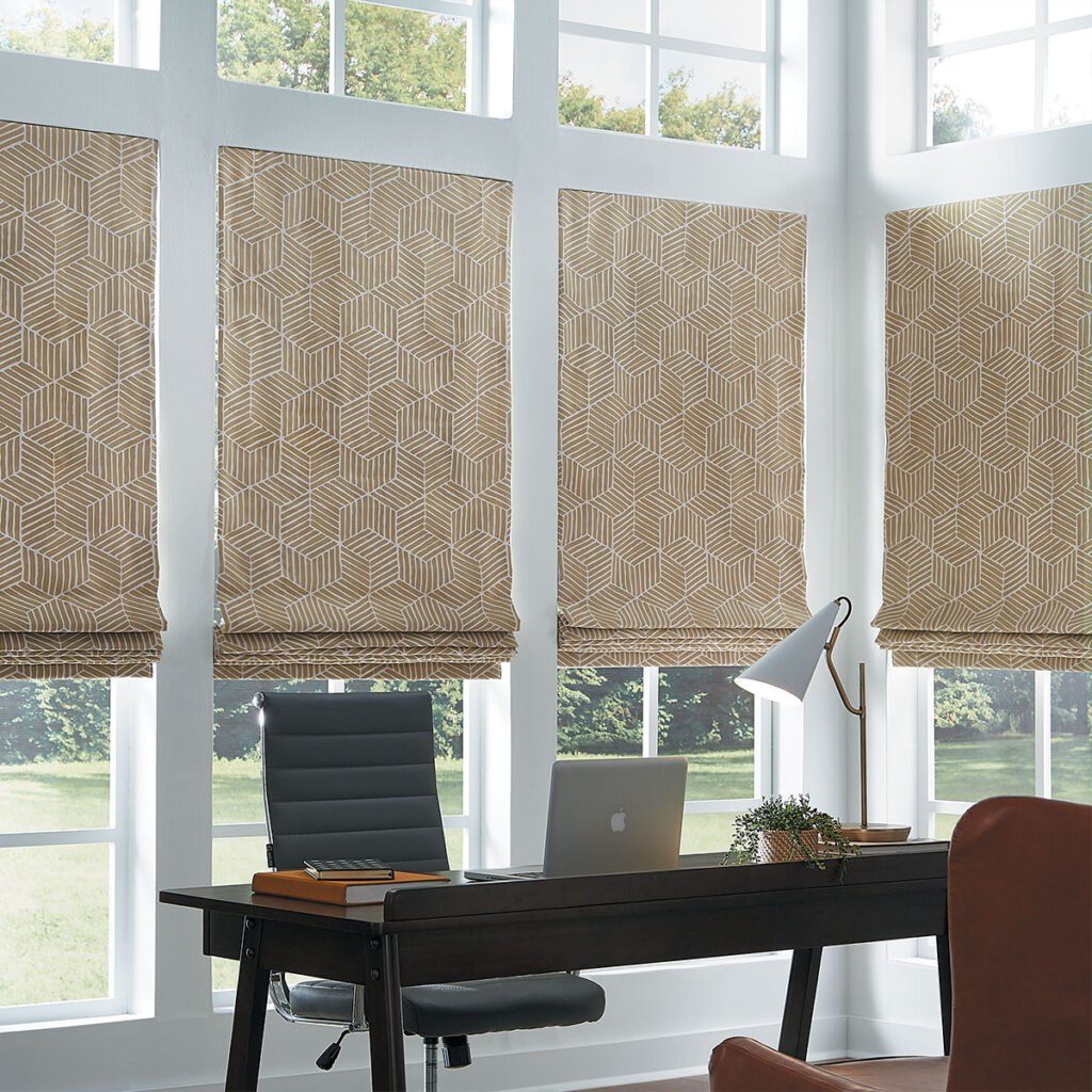 A wall of windows with partially opened Flat Roman Shades in a dark honey colored bold geometric pattern behind an office desk and chairs.