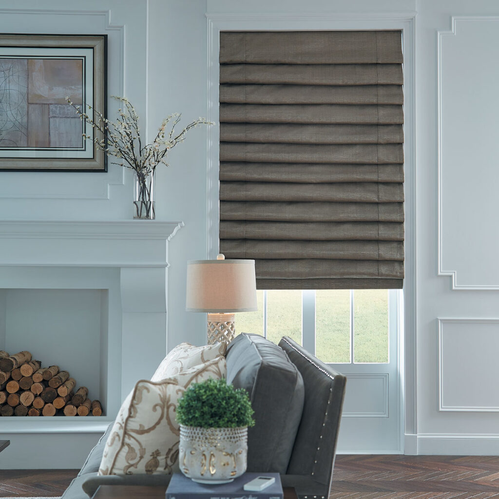 A Hobbled Roman Shade in a medium brown fabric with a little sheen on a window next to a fireplace in a living room.