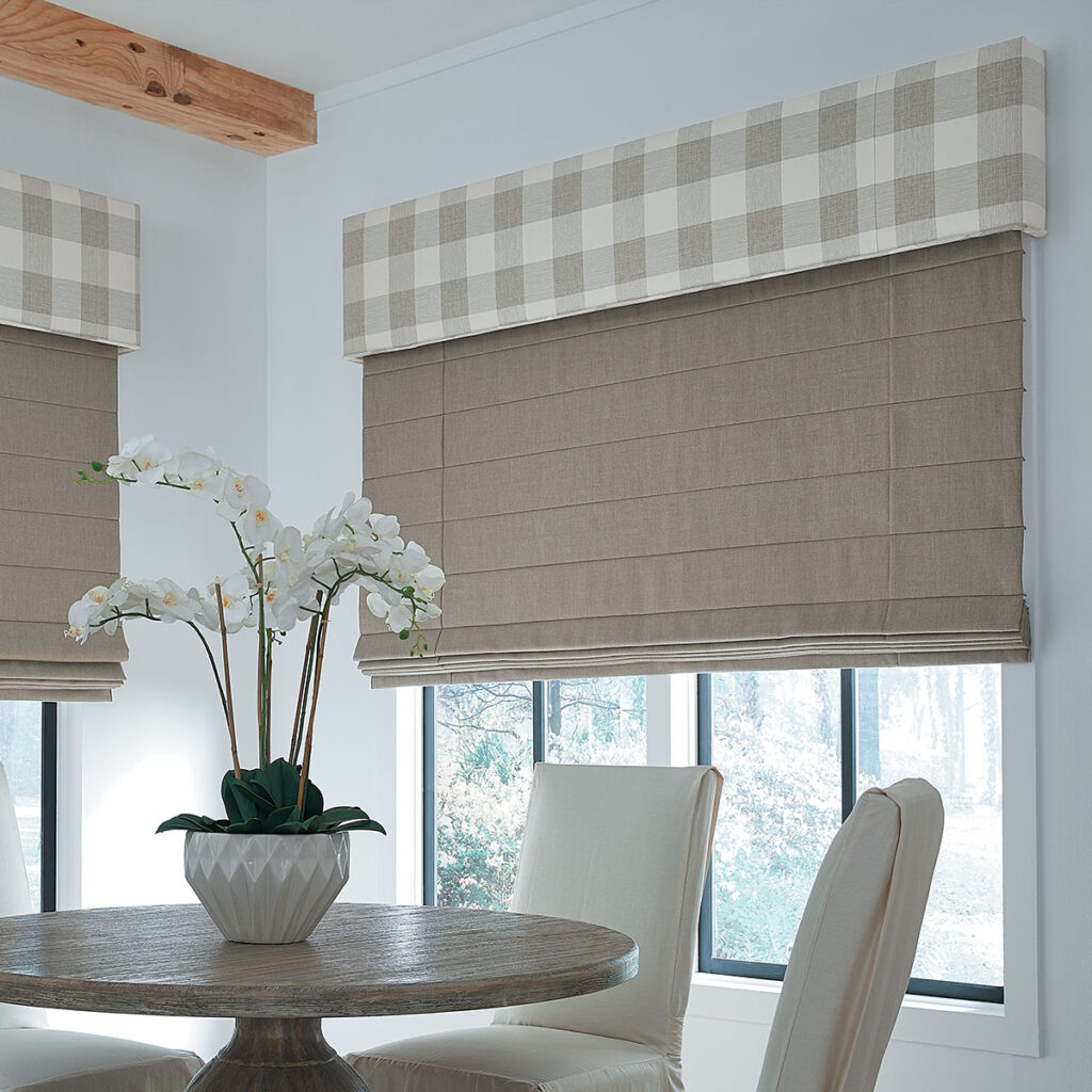 A white and warm neutral colored dining room with windows covered in beige Reverse Fold Roman Shades and large scale Buffalo check Statler Cornices in beige and off-white.