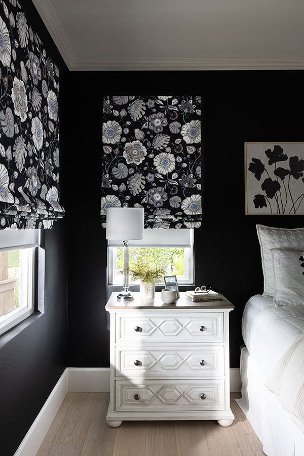 Soft Roman Shades with PowerView Automation in a black and white floral patterned fabric on two windows in the corner of a bedroom.