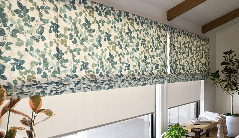 A wall of windows with PowerView Automation on soft Roman Shades with a blue and green leaf pattern.