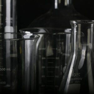 Dramatically lit glass chemistry containers on a dark background.