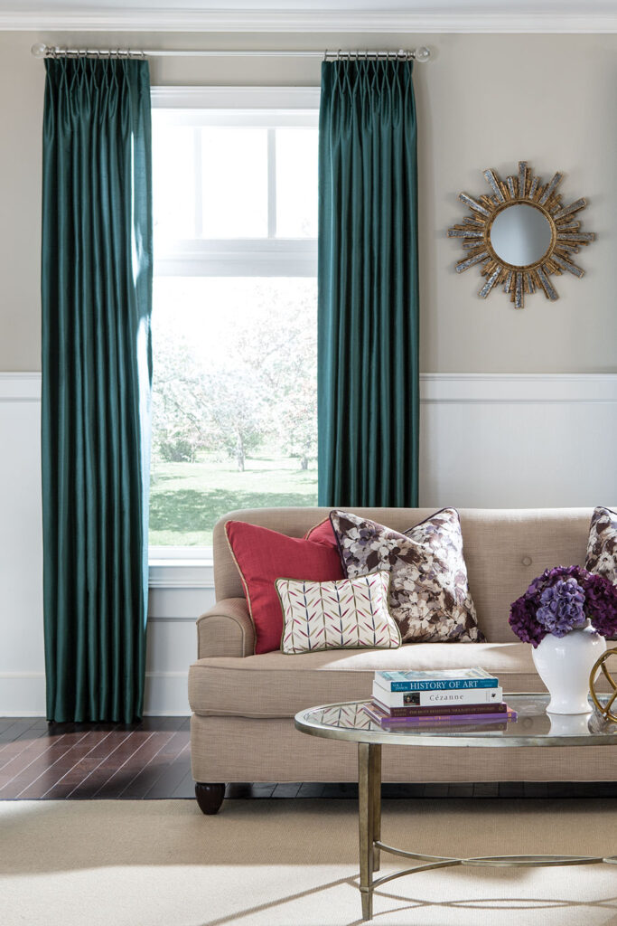 Monarch Pleat Drapery in dark teal on a window in a casual living room.