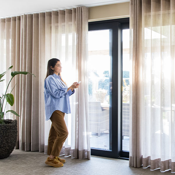 A woman standing in front of glass doors with drapery on Forest Motorized Drapery Hardware.