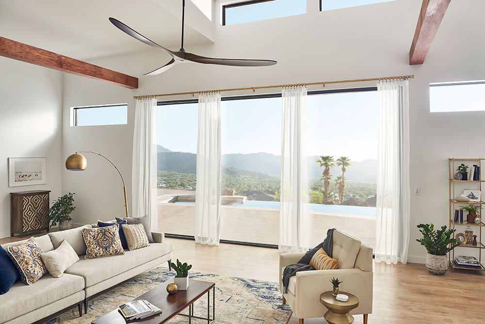 An open living room with sheer white drapery panels on Kirsch drapery hardware over a series of glass doors.