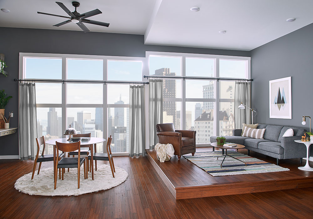 A modern great room in gray and dark wood featuring a wall of windows with Kirsch drapery hardware over light gray sheer drapery panels.