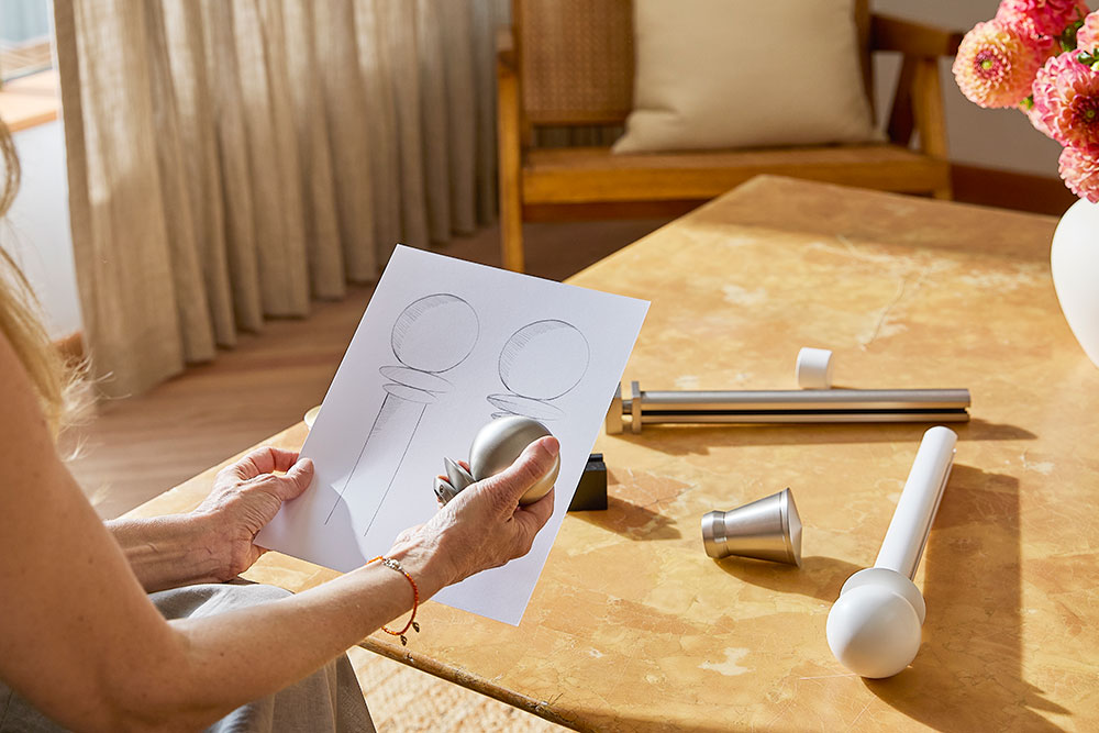 A woman's hands as she holds sketches of PowerView Motorized Drapery Hardware finals next alongside hardware pieces.