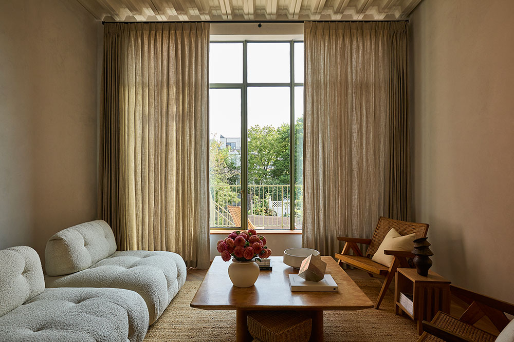 A wall of windows in a shadowed warm neutral room featuring beige Olivia Pleat Drapery on PowerView Motorized Drapery Hardware.