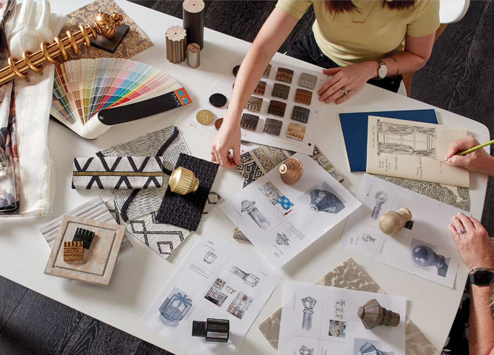 Looking down onto a table covered with sketches and components from Paris Texas Hardware as two sets of hands reach in to create designs.