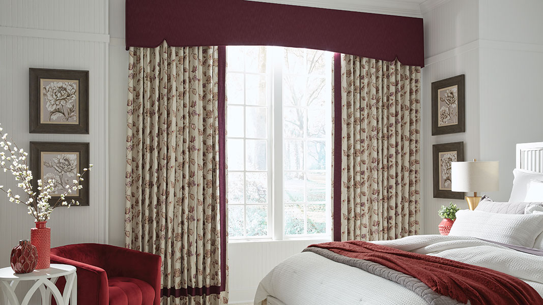 A traditional bedroom featuring custom drapery in a pattern of red and ivory leaves and a cornice in a coordinating red fabric.